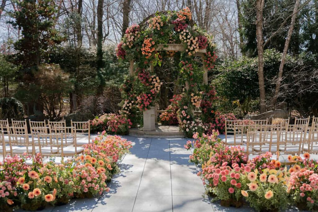 Over-the-top luxury fresh floral ceremony installation by Intrigue Designs at Crystal Plaza in New Jersey, featuring lush blooms, romantic garden-style arrangements, and a dramatic aisle lined with florals.