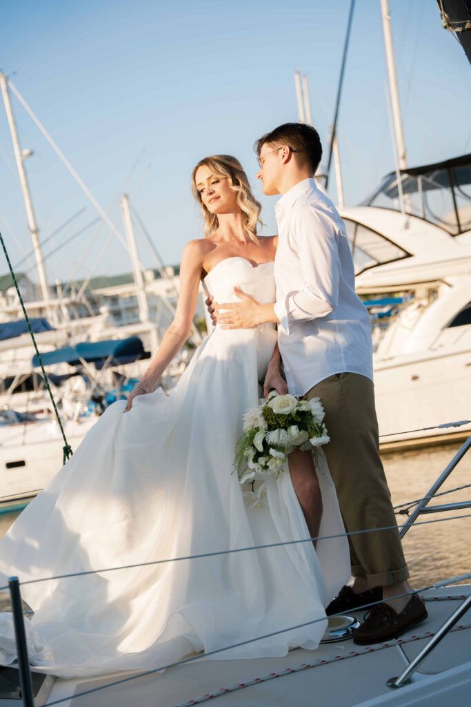 Stephanie and Charlie standing on a sailboat during golden hour, with the Charleston skyline in the background.