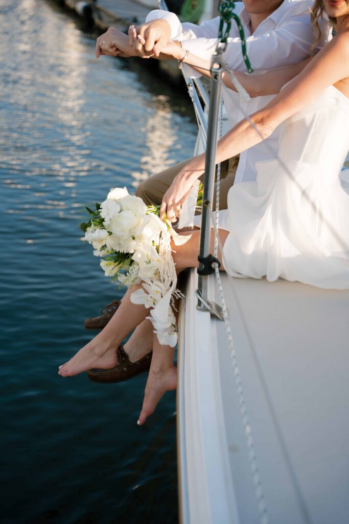 Modern bridal bouquet with soft florals and greenery resting on sailboat deck, styled for a coastal elopement. Florals by Fire Fly Wed