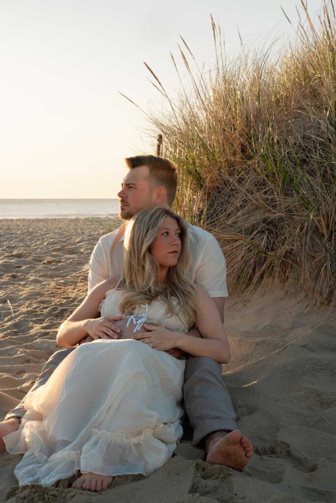 Couple sitting on the beach during sunrise for a maternity session at Spring Lake Beach in New Jersey